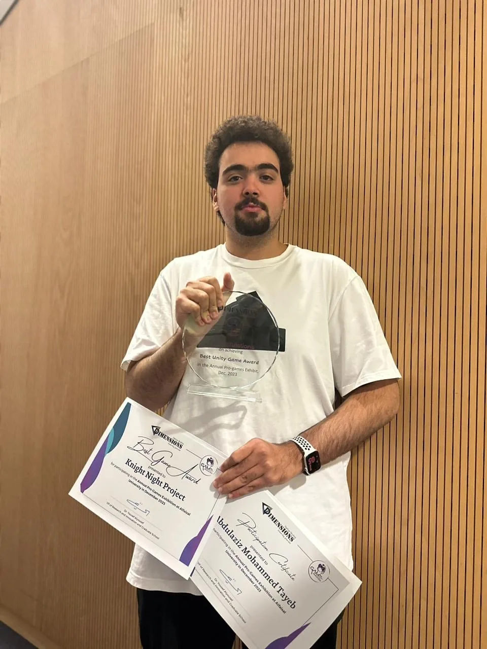 Abdulaziz holding the Best Unity Game trophy and certificates